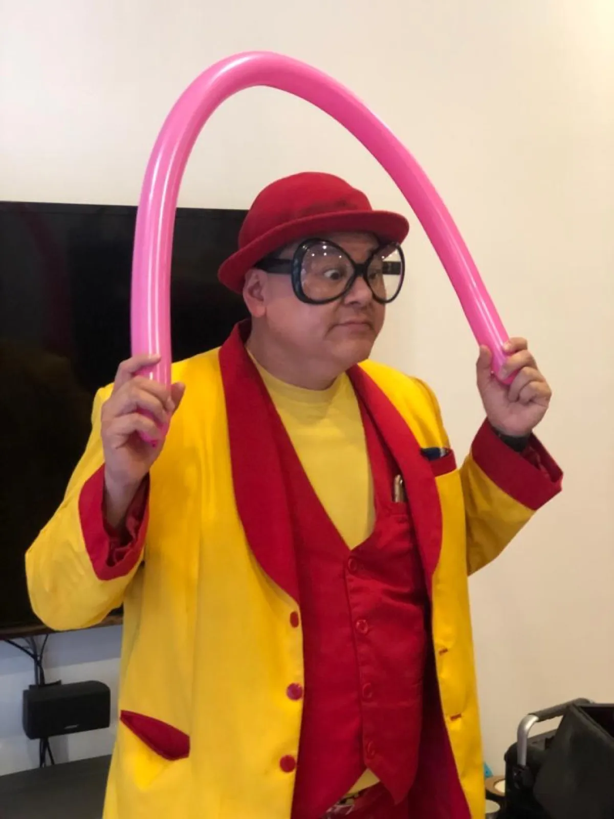 Close-up of Maddie in his red hat and oversized glasses holding a pink balloon sculpture