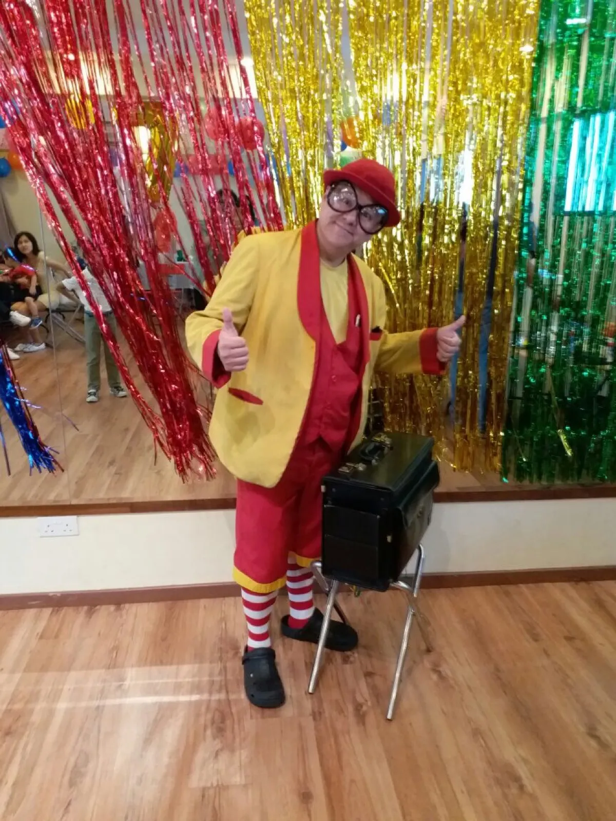 Maddie in his yellow jacket and red hat giving two thumbs up beside his magic case